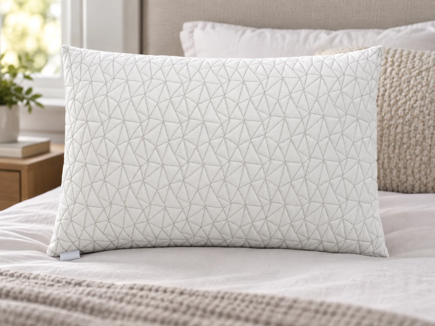 White pillow with a quilted geometric cover on a bed.